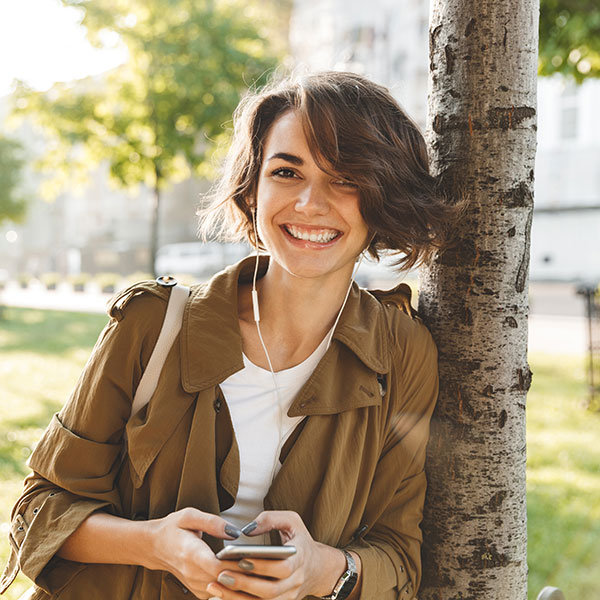 Woman with Phone Smiling by Tree